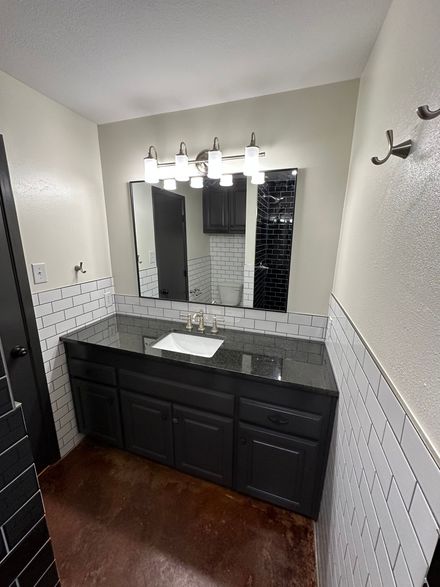 Modern bathroom with dark vanity, white tile walls, mirror, and three light fixtures
