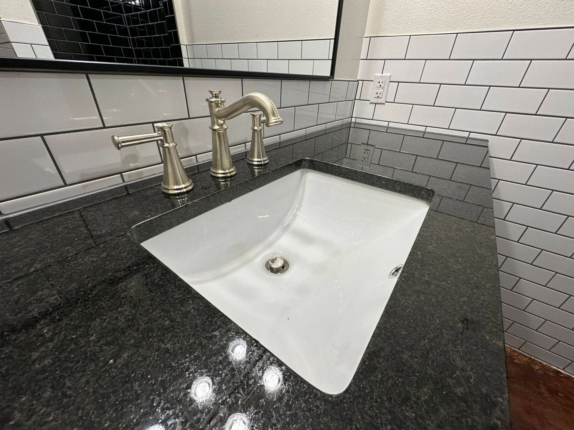 Granite bathroom vanity with white sink, brass faucet, and subway tile backsplash