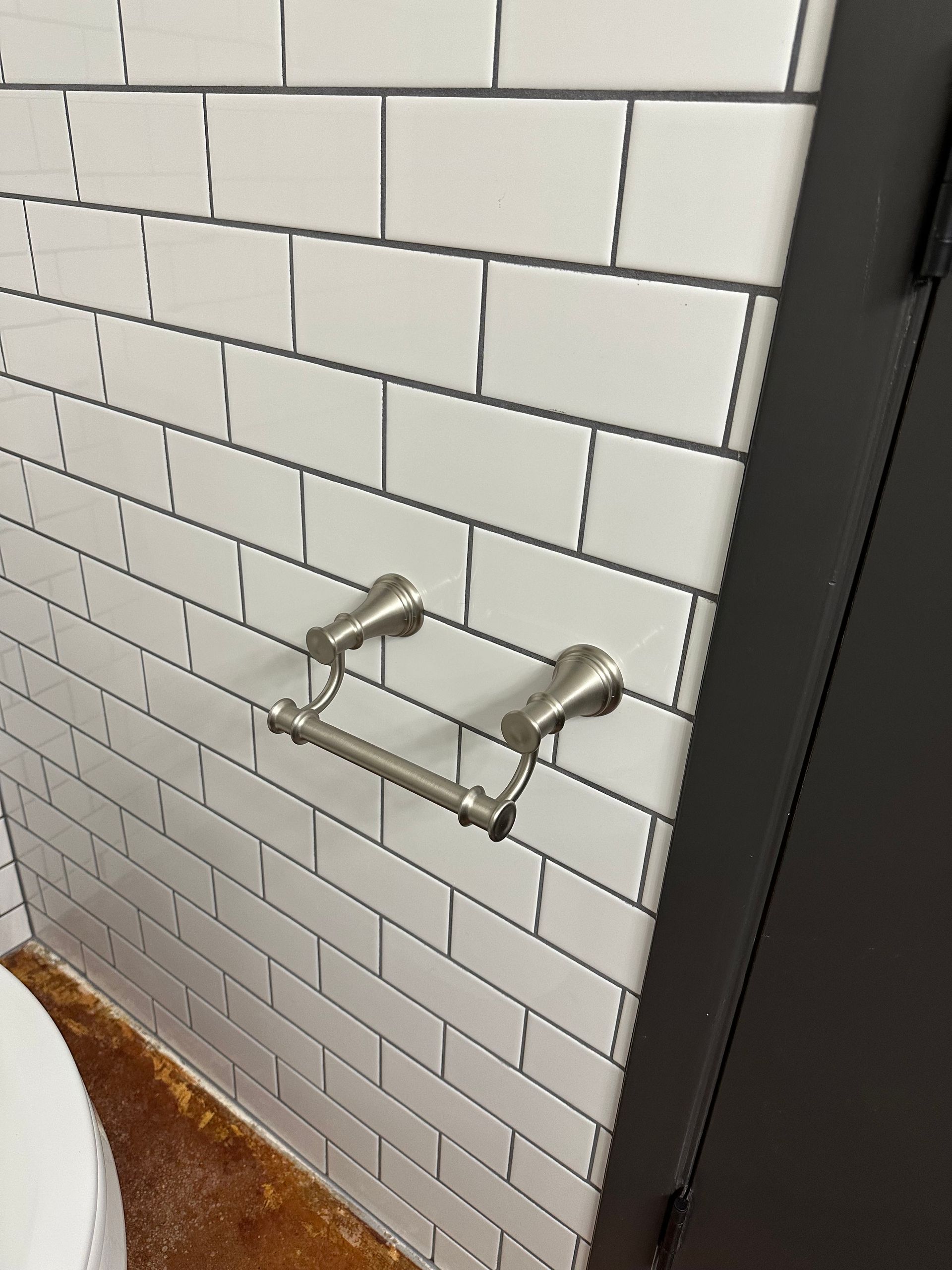 Two chrome toilet paper holders mounted on a white subway-tile bathroom wall