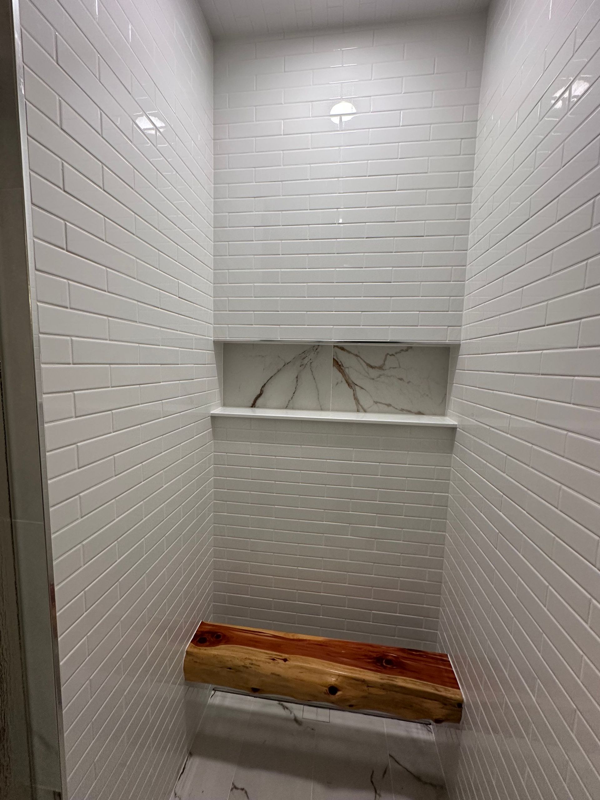 White tiled shower with a built-in niche and a wooden bench seat.
