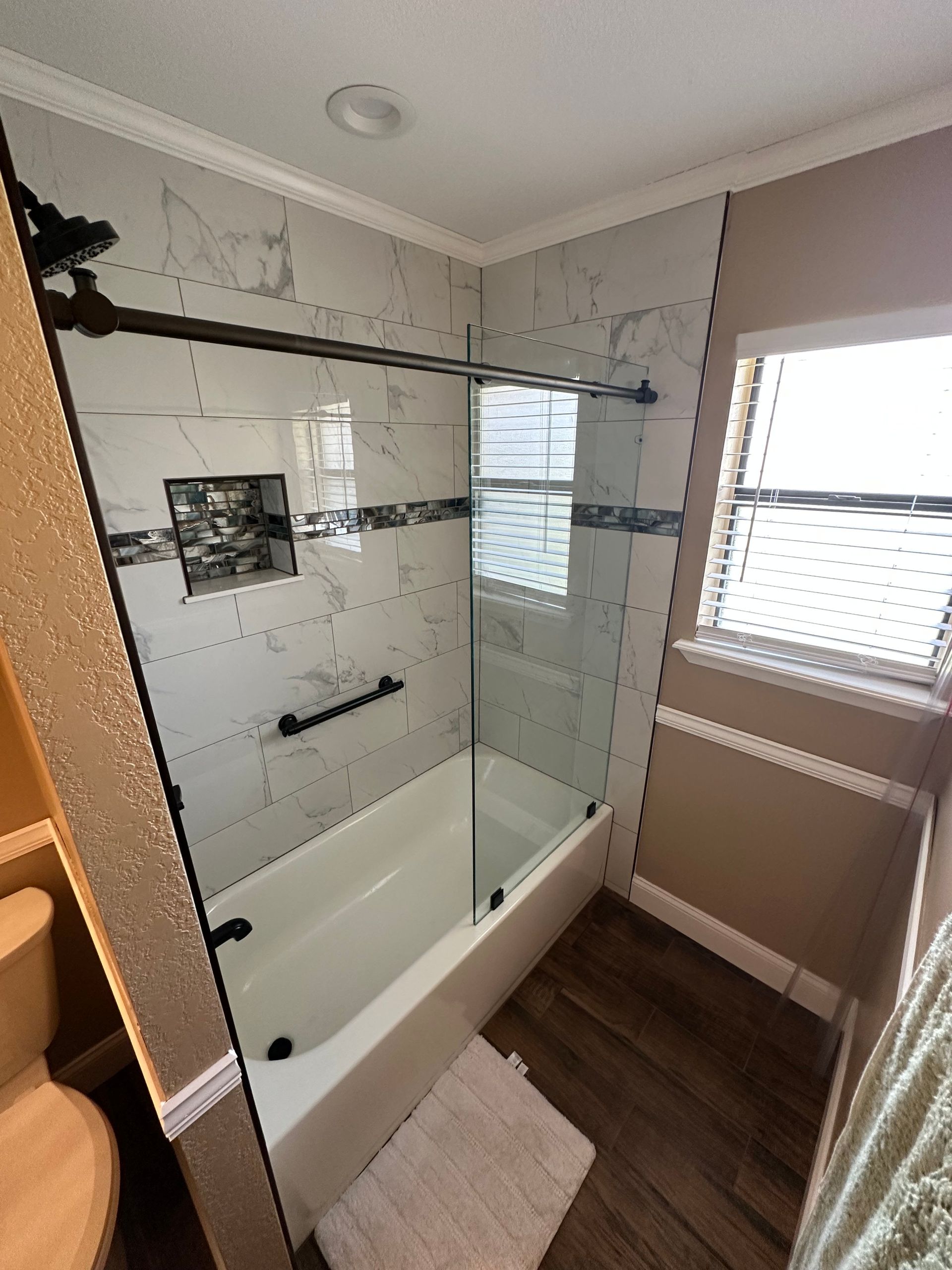 Modern bathroom with glass shower-tub combo, wood floor, and window light