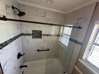 Empty white tiled bathroom shower with bench, grab bars, and window blinds