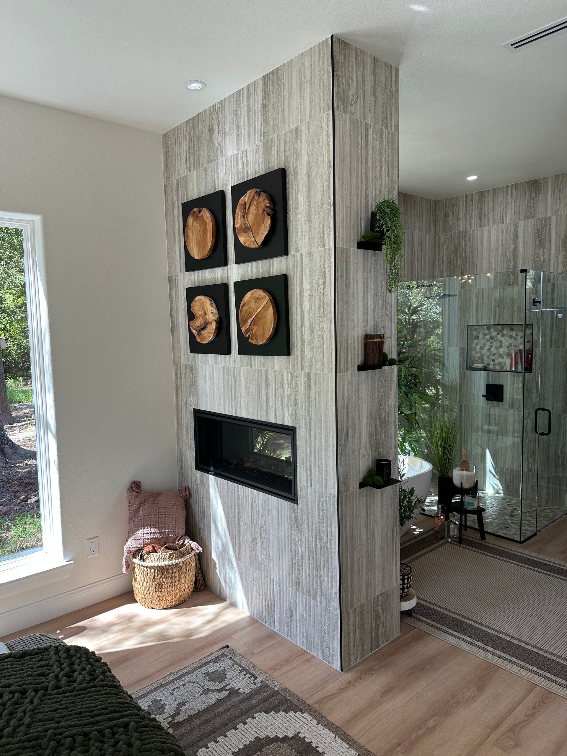 Modern living room with a tiled fireplace wall, framed art, glass shower, and natural light.