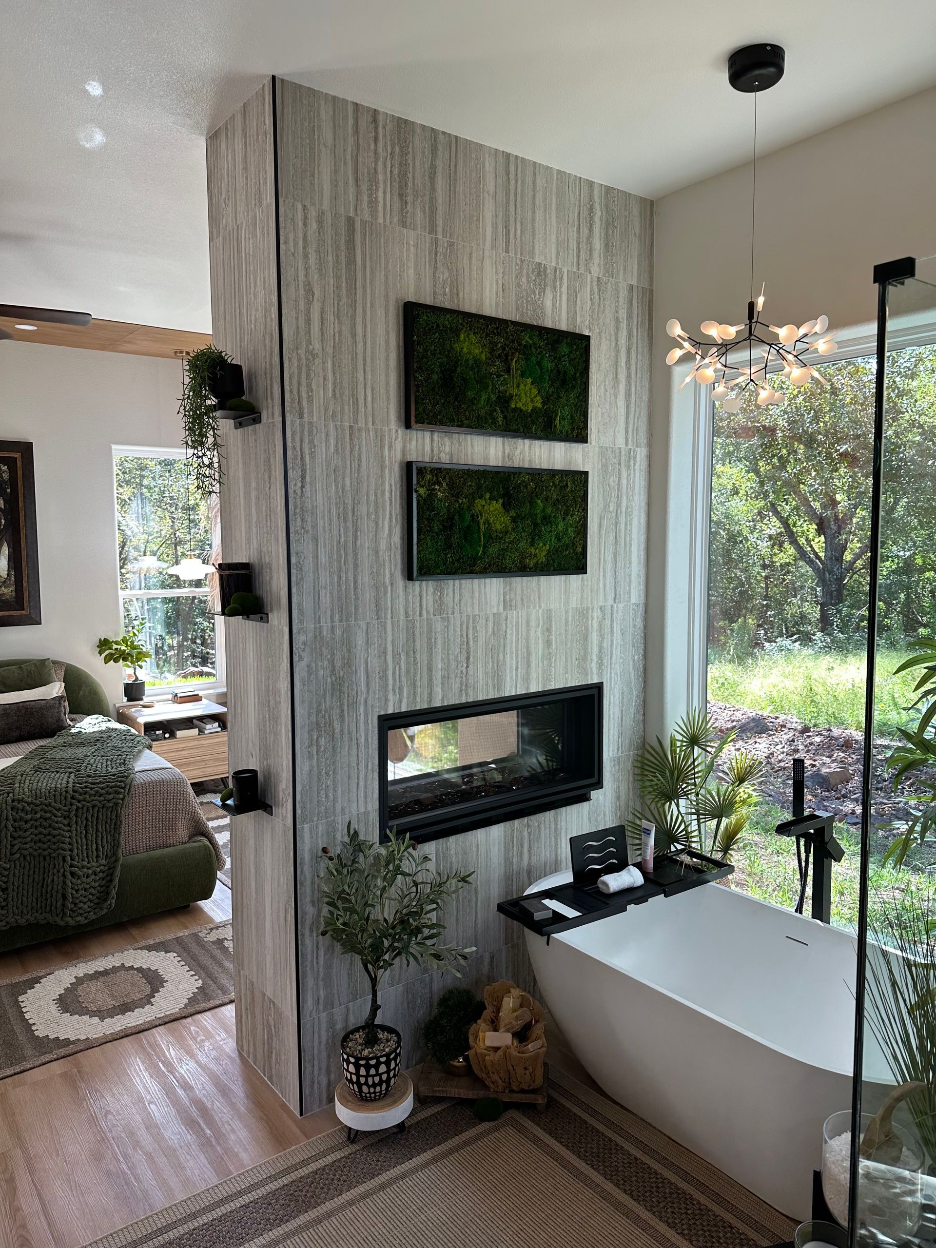 Modern living room with a concrete fireplace, wall art, and a white bathtub by a large window with greenery outside