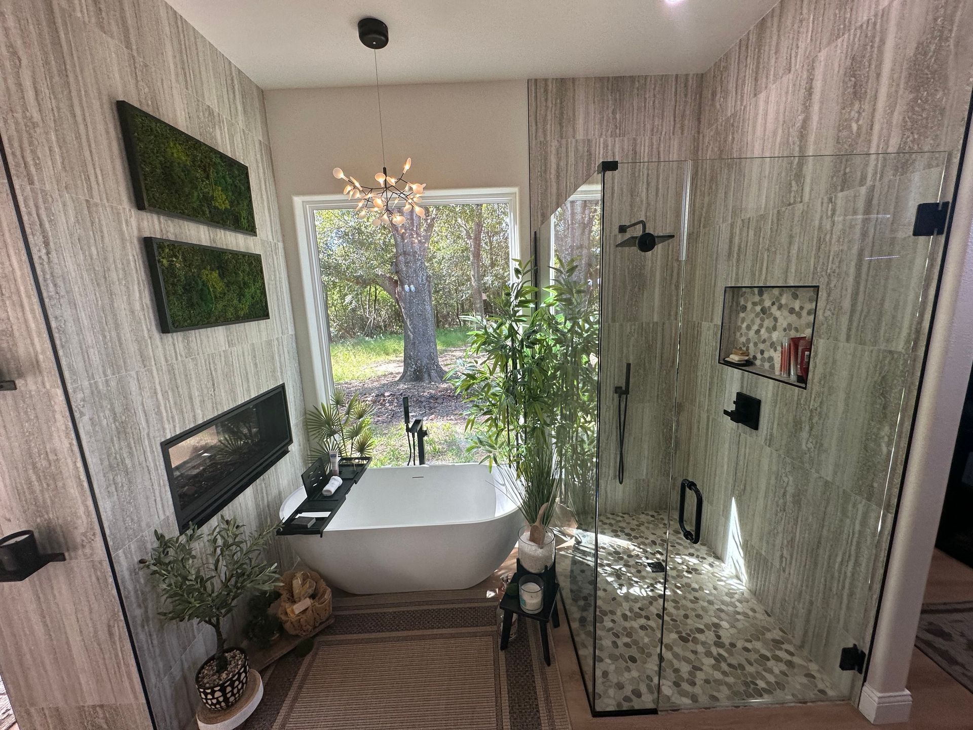 Modern bathroom with freestanding tub, glass shower, and large window overlooking greenery
