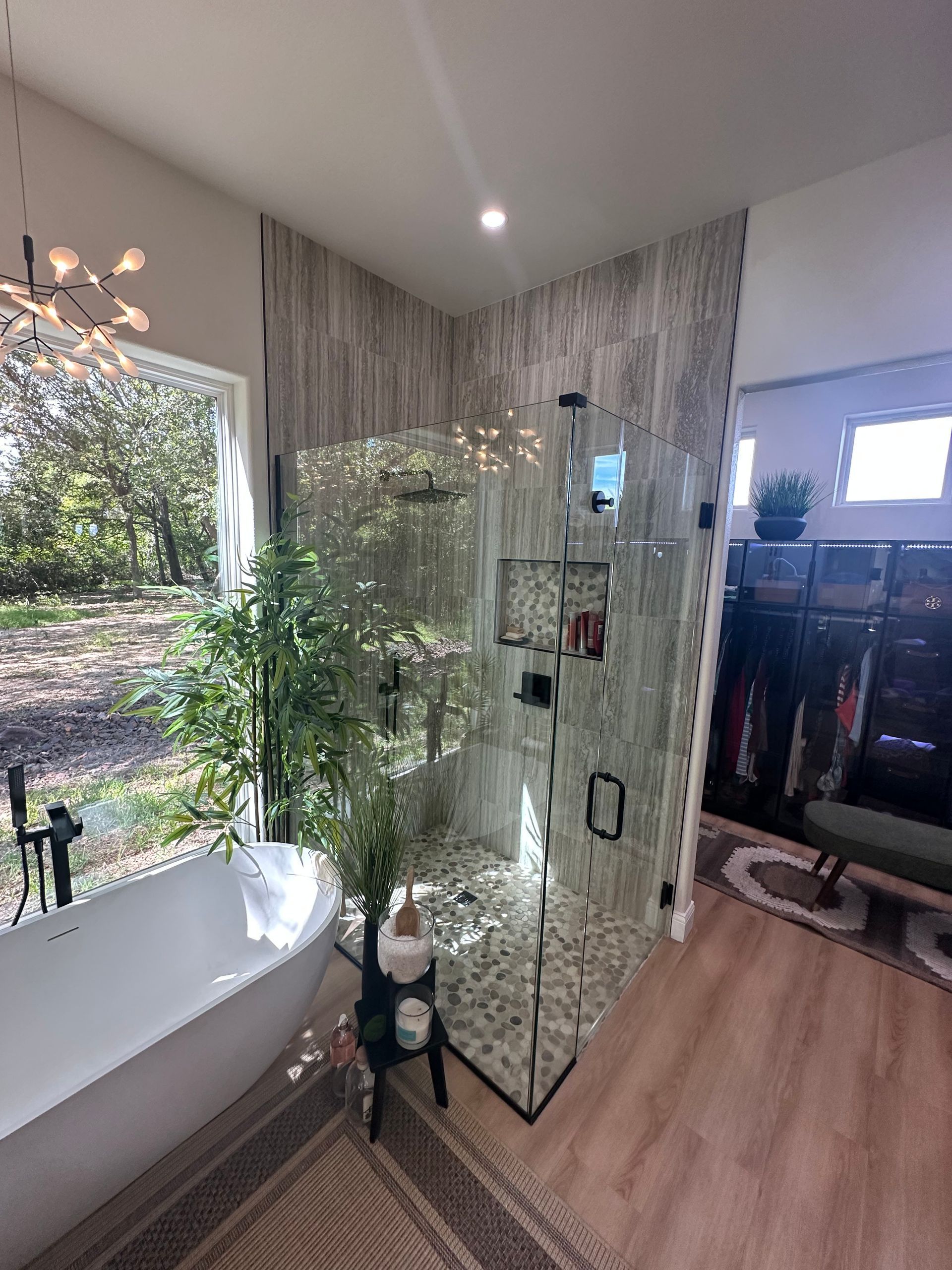 Modern bathroom with a freestanding tub, glass shower, and a tall plant by a large window.