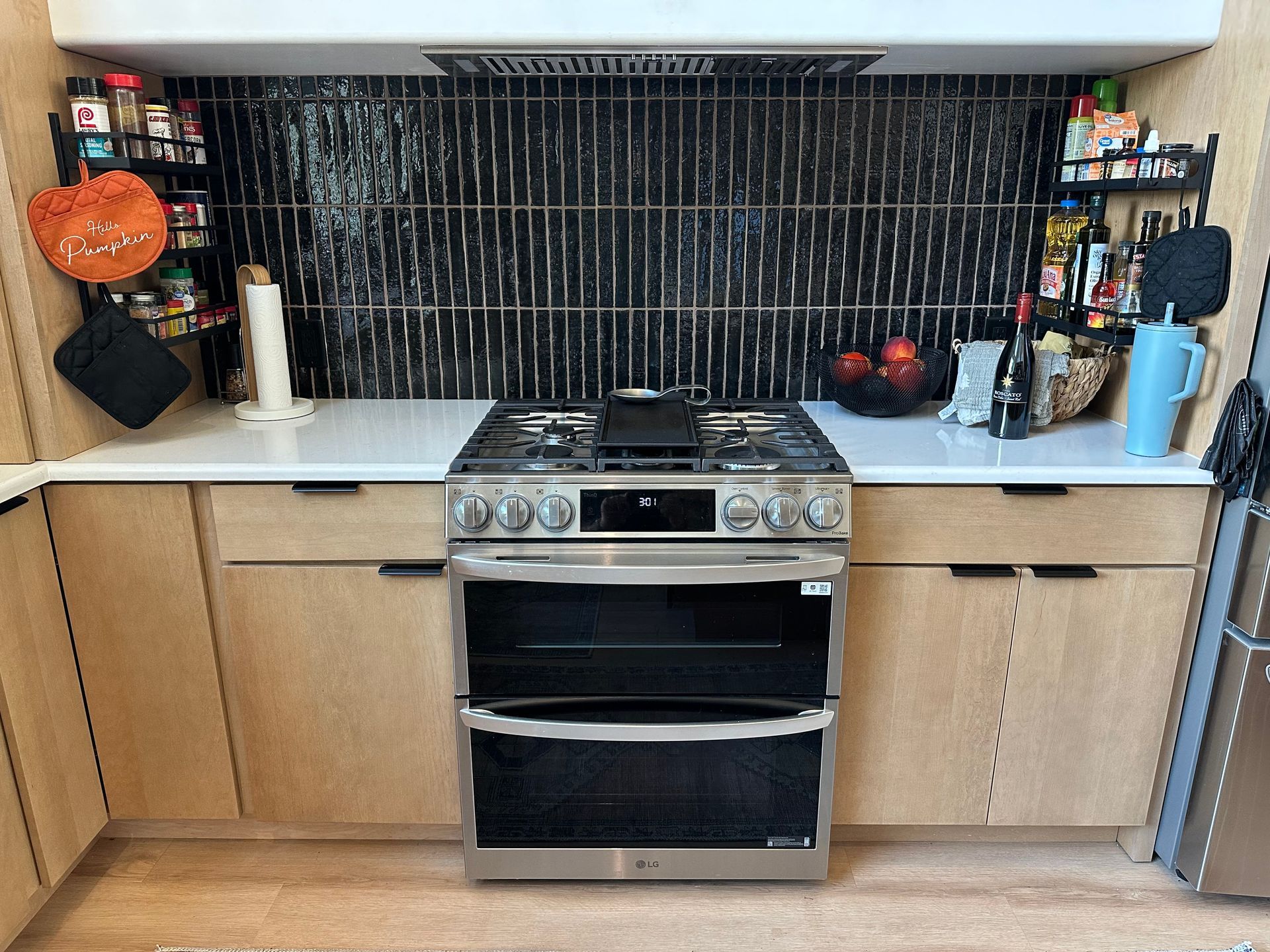 Compact kitchen with stove centered between wood cabinets and a black tile backsplash, countertops with small items.