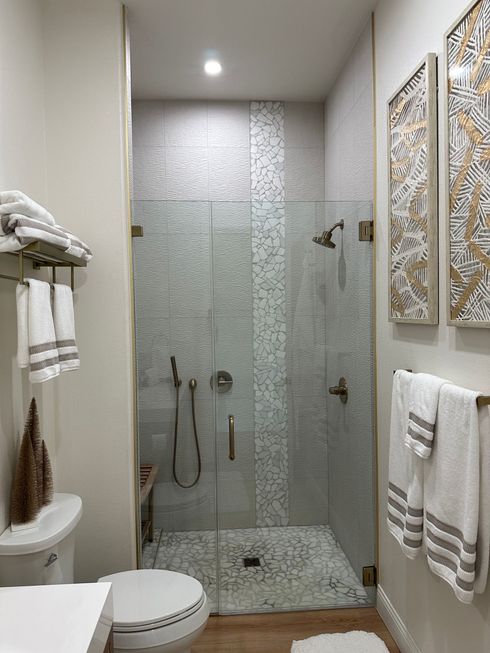 Small bathroom with glass shower, white towels, toilet, and framed wall art.