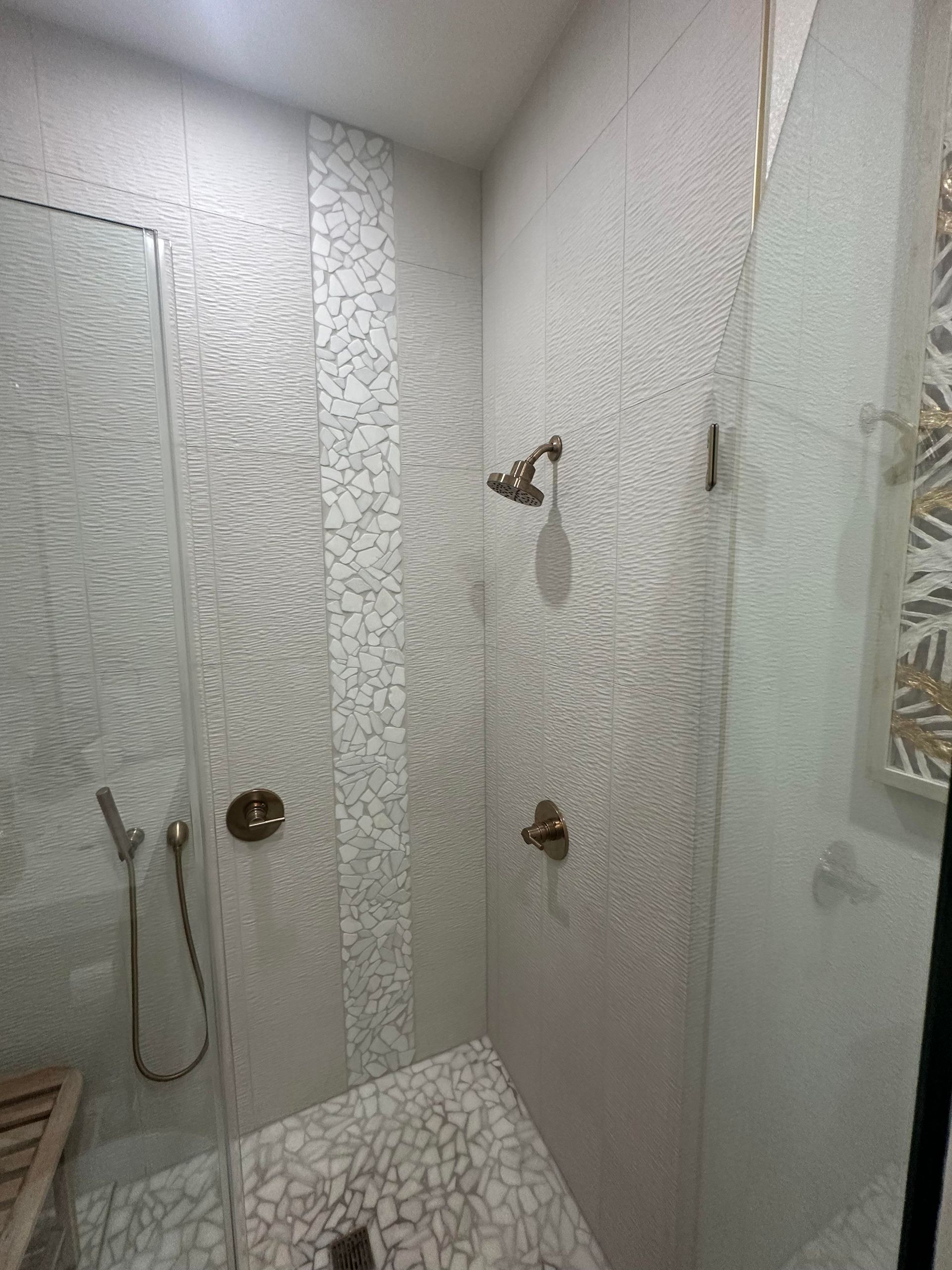 Small tiled shower with glass door, two showerheads, and a built-in bench.