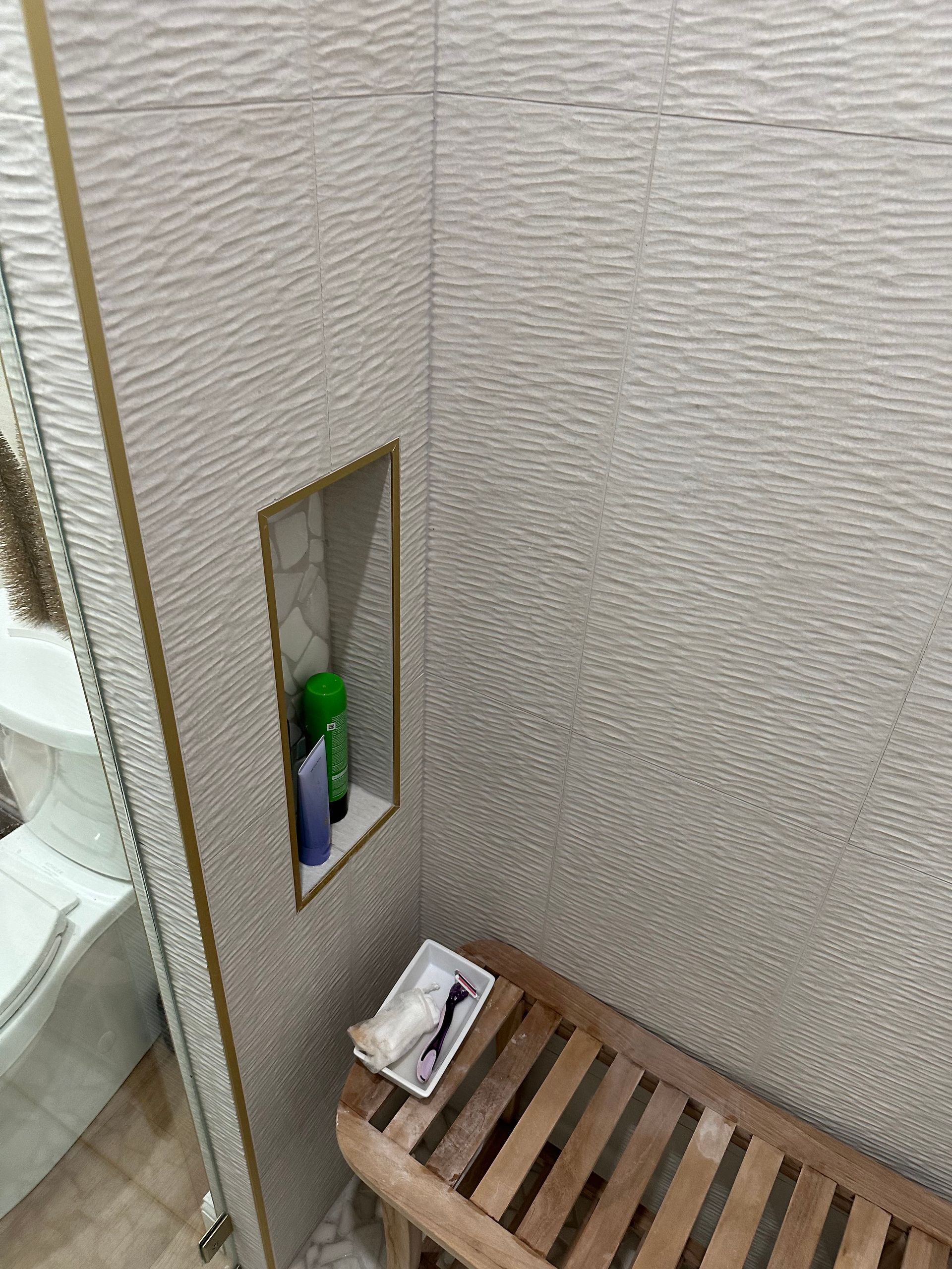 Small bathroom corner with a narrow wall shelf holding toiletries and a wooden slatted stool below.