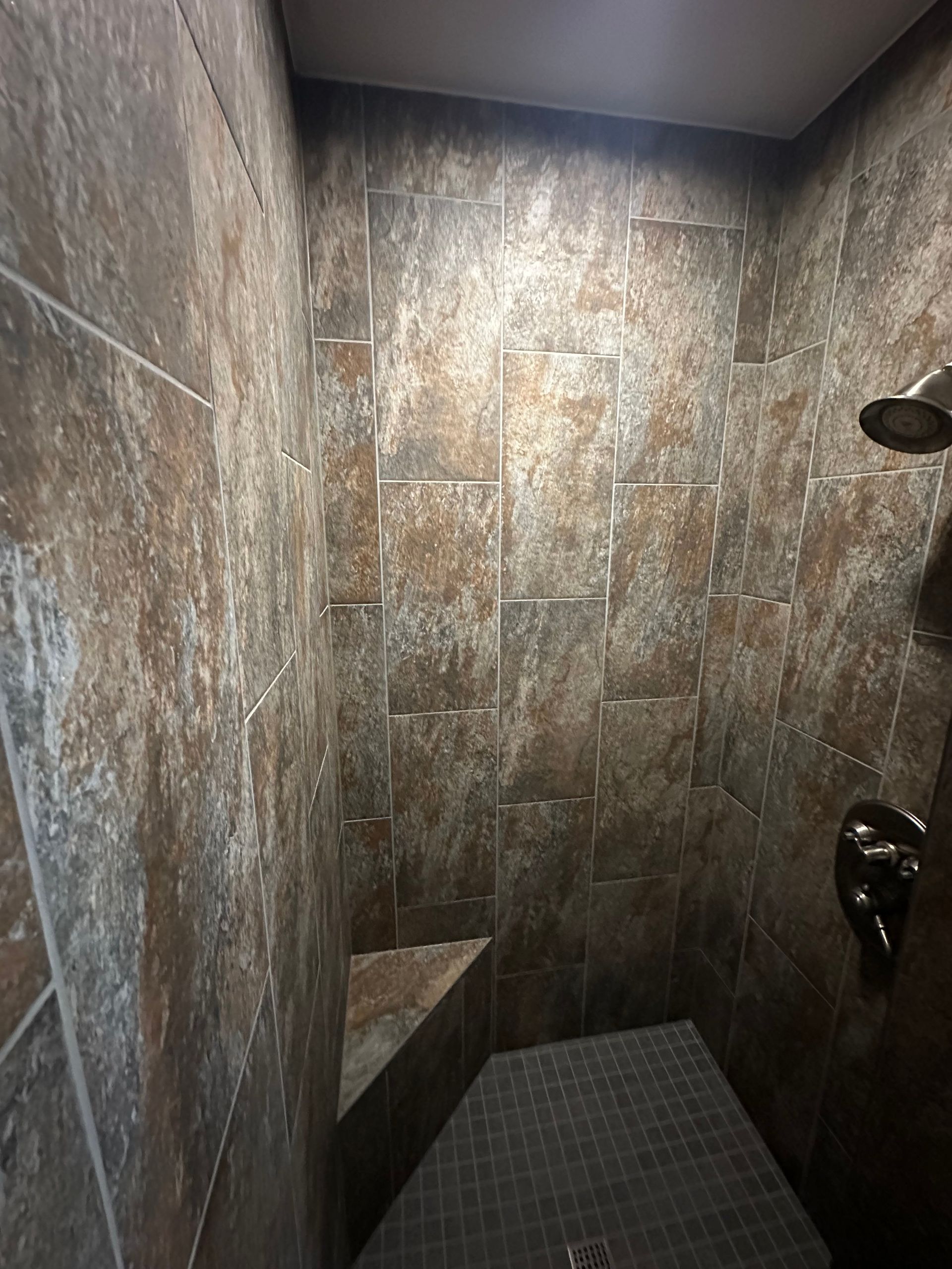 Tiled shower stall with stone-look walls, dark fixtures, and a small floor drain area.