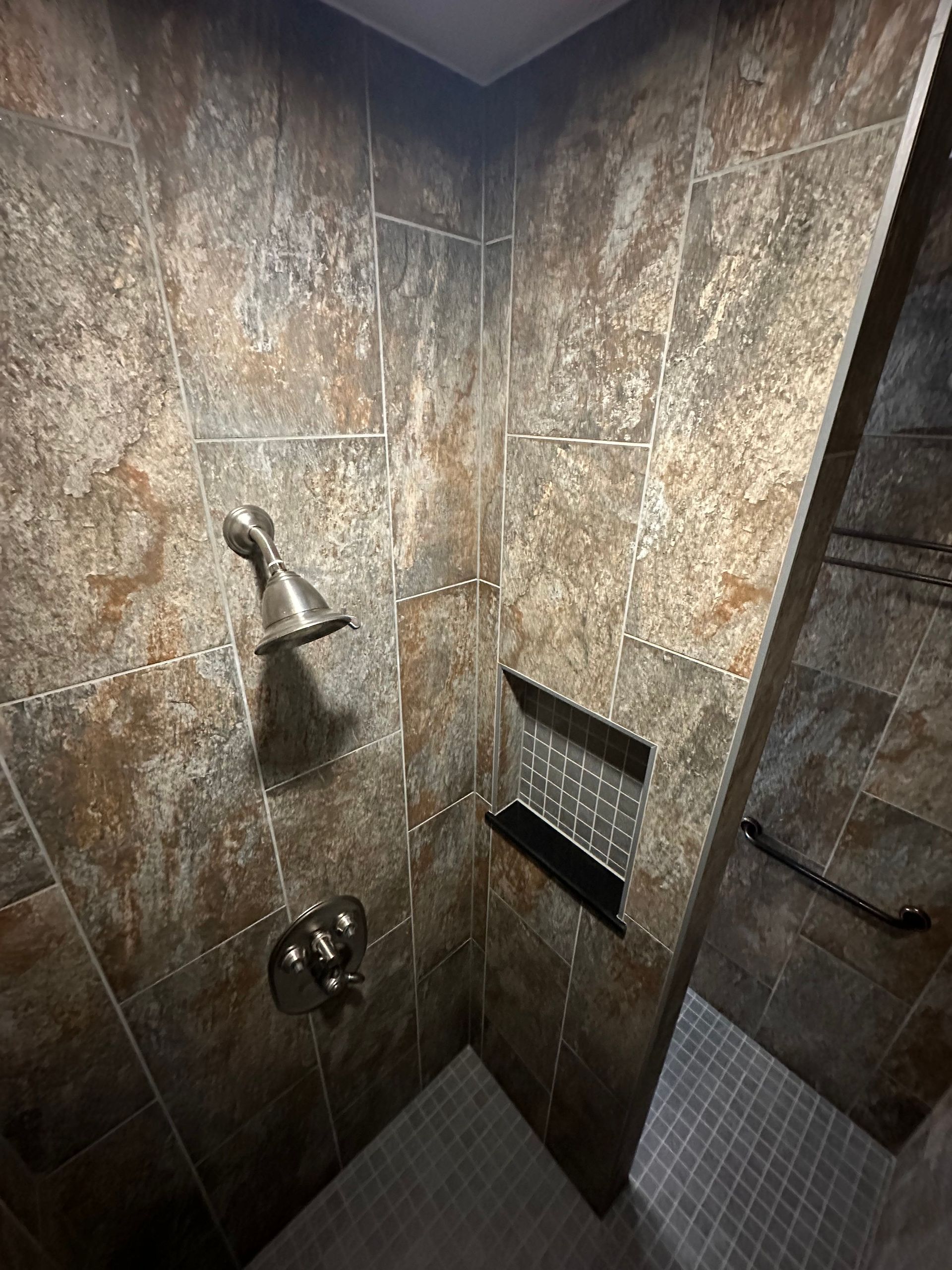 Walk-in shower with brown tiled walls, chrome fixtures, and built-in shelves
