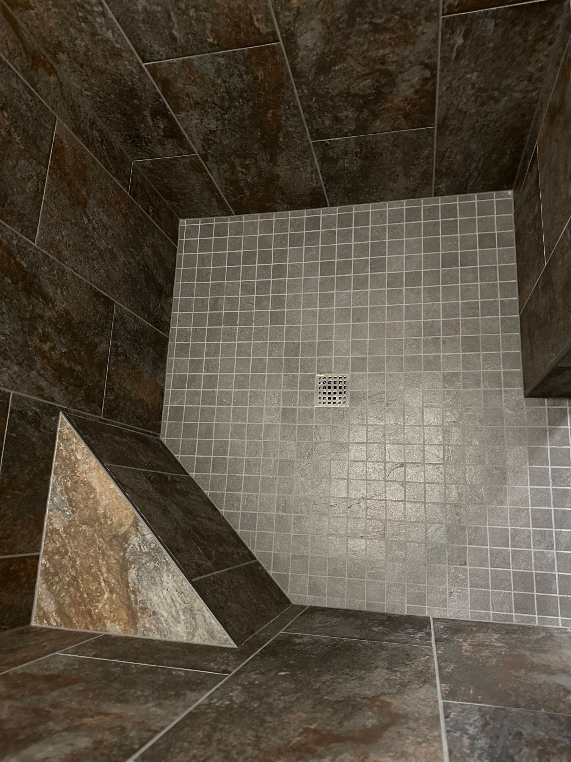 Empty tiled shower stall with a square drain and dark stone walls.
