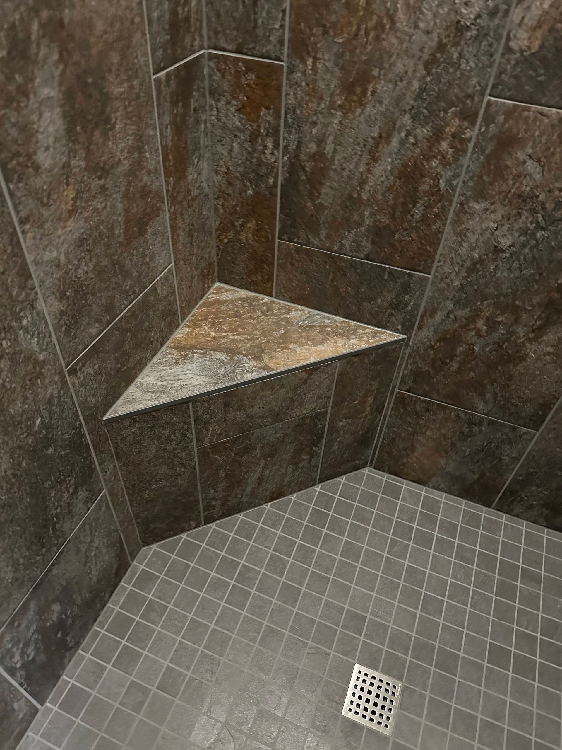 Tiled shower corner with triangular stone shelf and floor drain