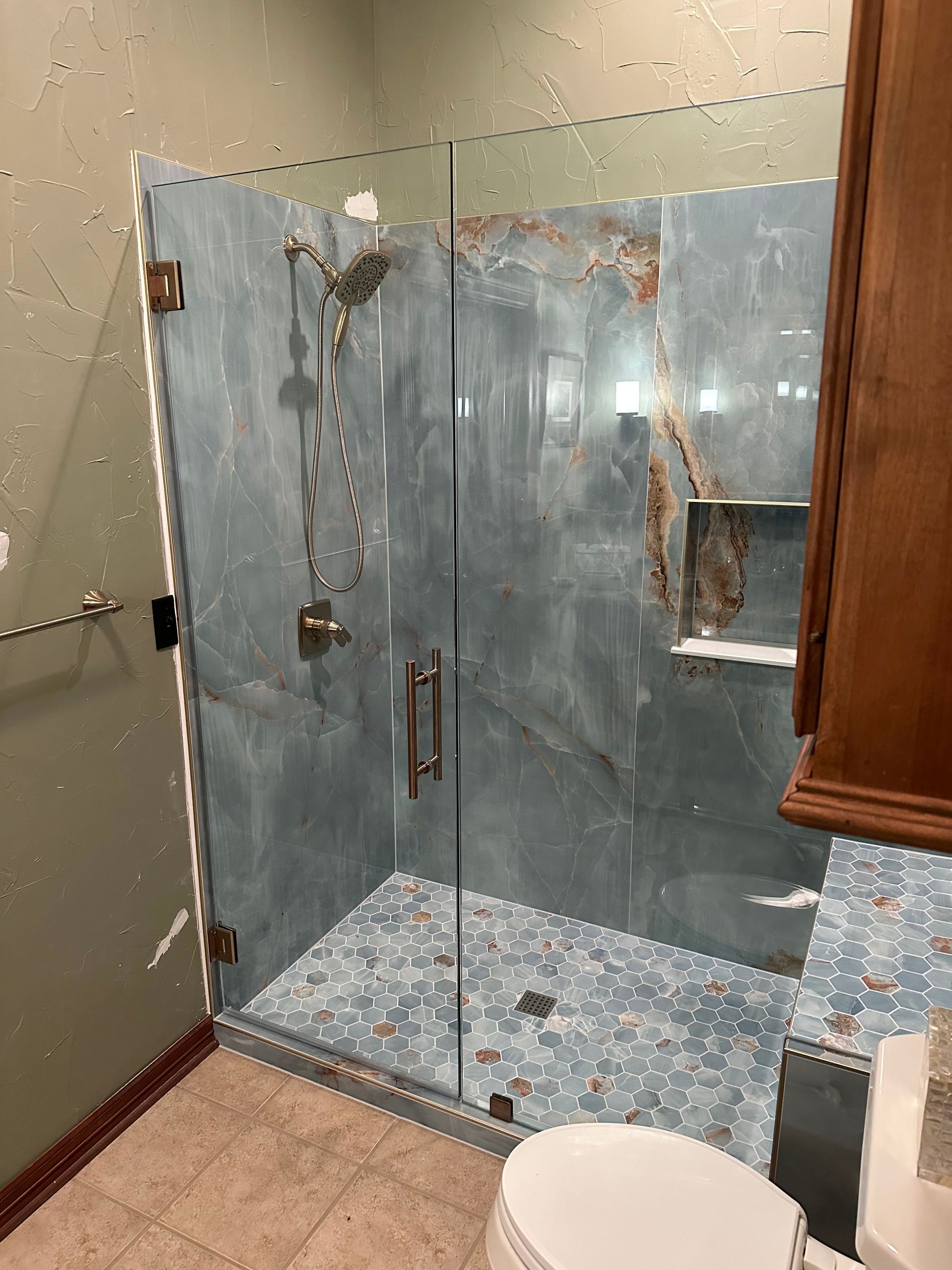 Bathroom with glass-enclosed shower, blue mosaic tile floor, beige walls, and a white toilet in the foreground
