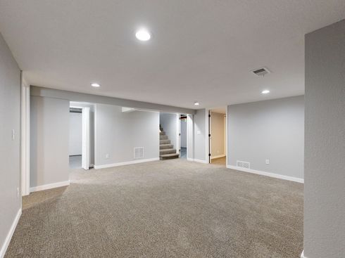 Empty carpeted basement with gray walls, recessed lights, and stairs leading upstairs