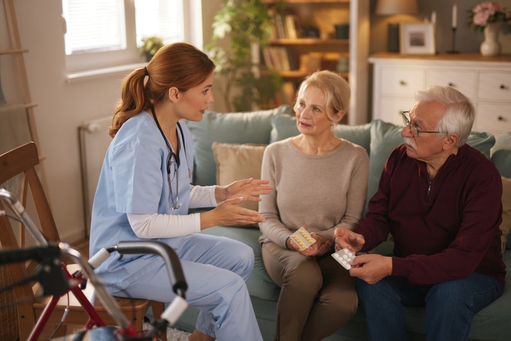 A healthcare provider consults with an elderly couple on a sofa; medication is visible.