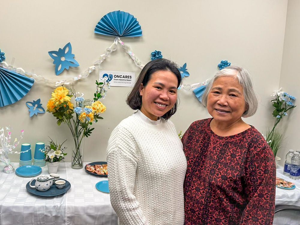 Two women smiling, posing in front of a decorated table with flowers and refreshments.