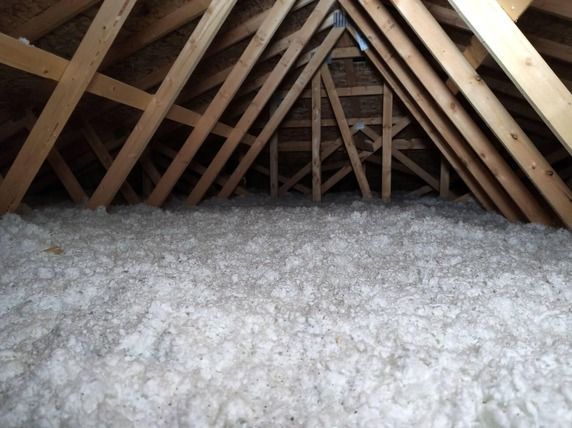 Attic with exposed wooden rafters and thick white insulation covering the floor
