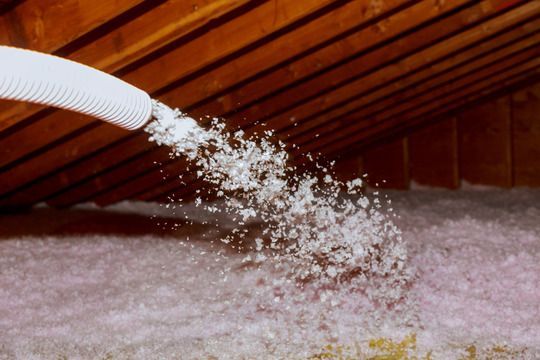 White hose blowing insulation into an attic with a sloped wooden roof