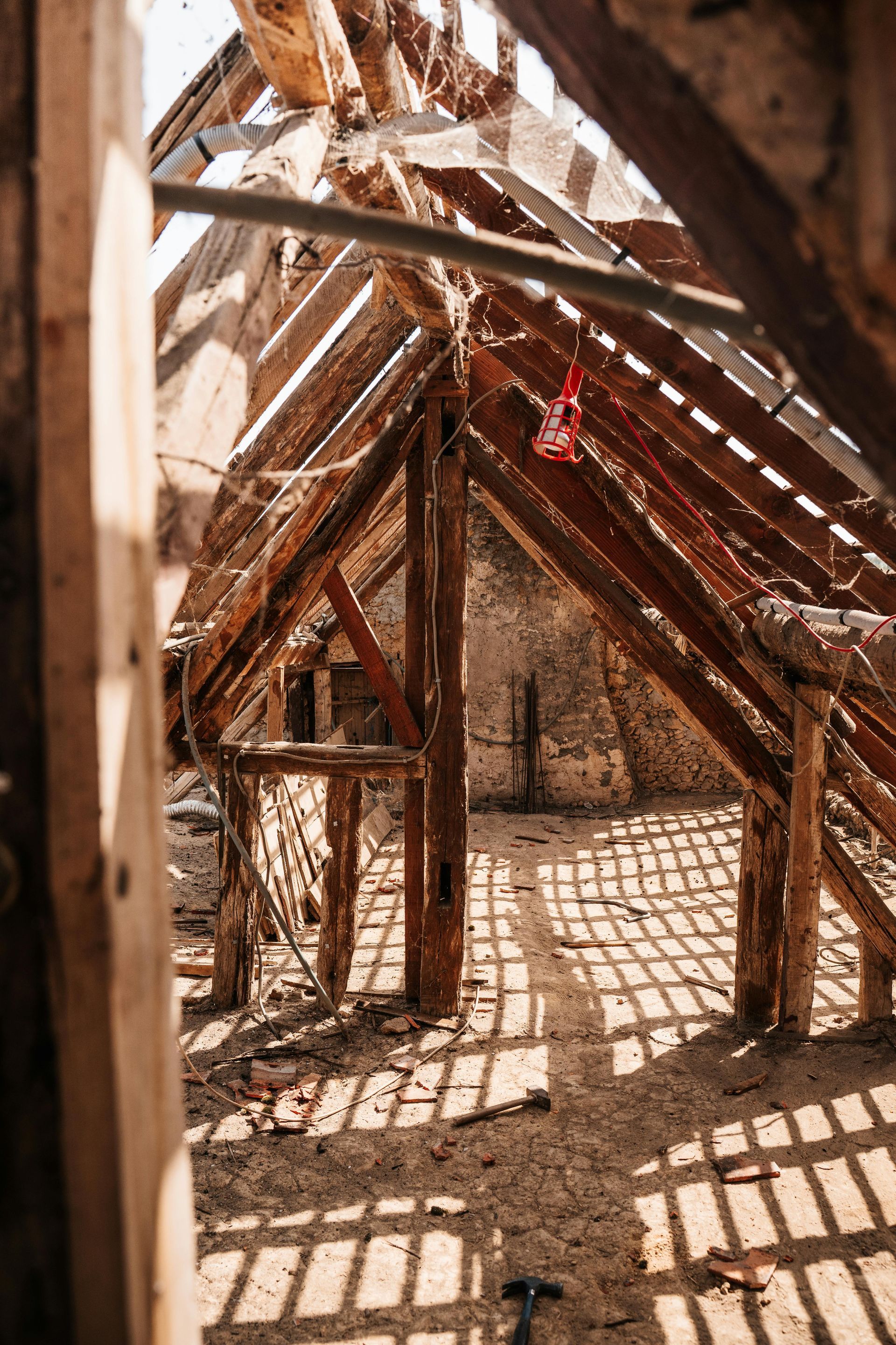 Sunlit wooden frame structure under construction, casting striped shadows on the ground.