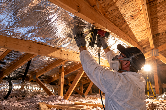 Technician stapling reflective radiant barrier foil to attic rafters in a Pasadena home