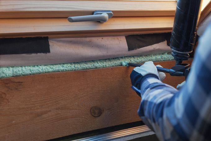 Person sealing insulation near a window