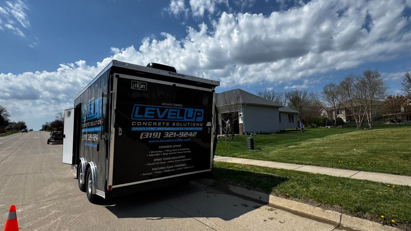 Black trailer parked on street with LEVEL UP logo, house in background, blue sky.