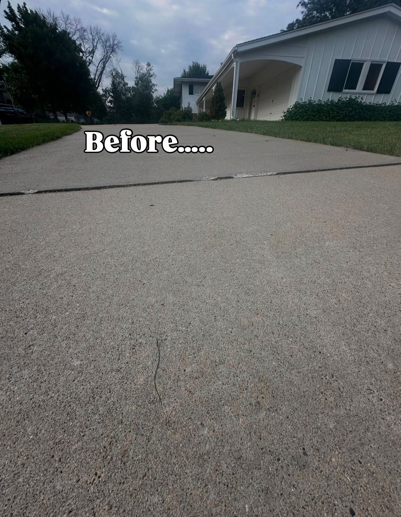 Driveway before repair, with visible cracks. House and trees in the background under a cloudy sky.
