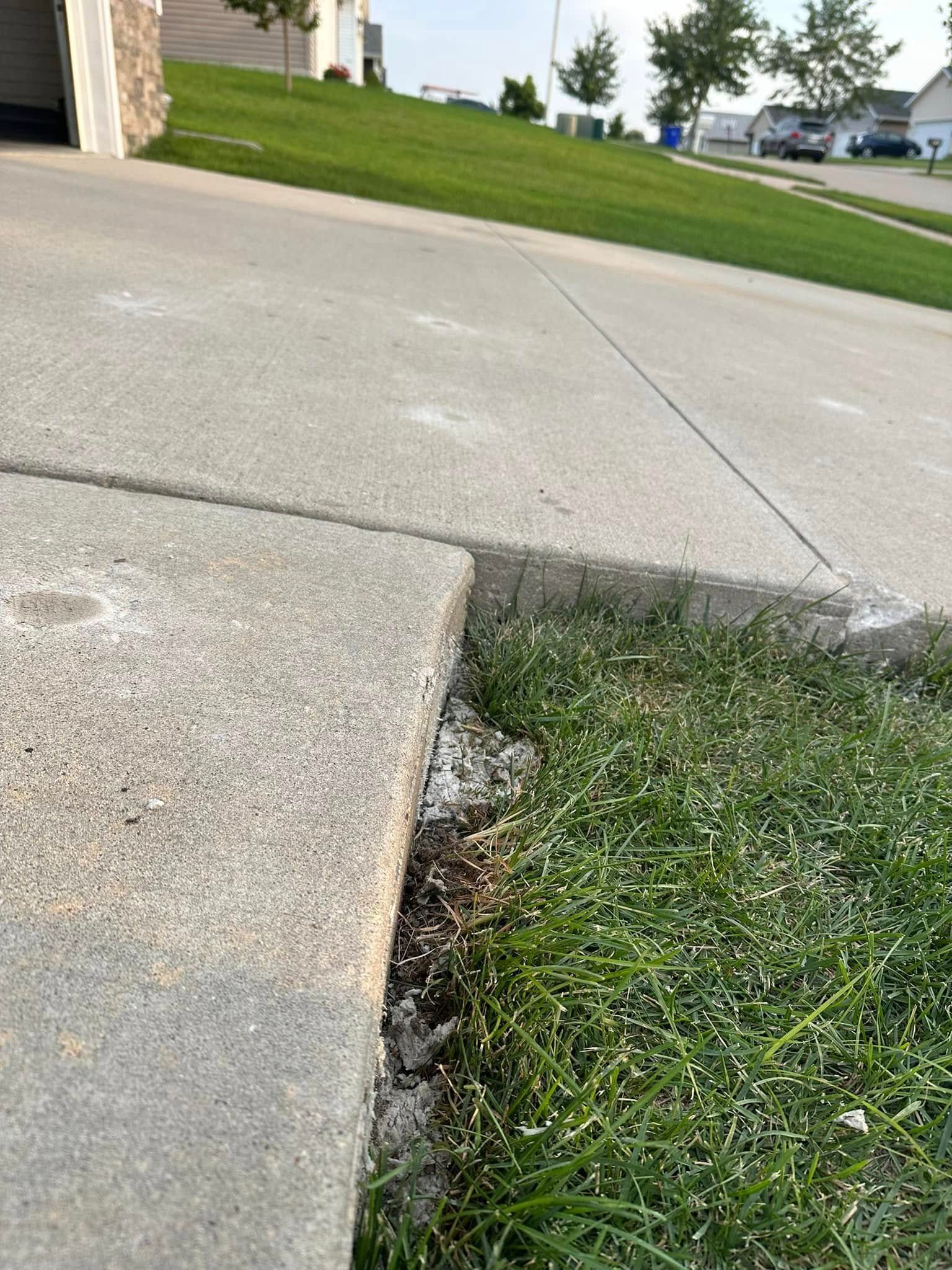 Concrete driveway and sidewalk edge next to grass. White substance present on the grass and concrete.