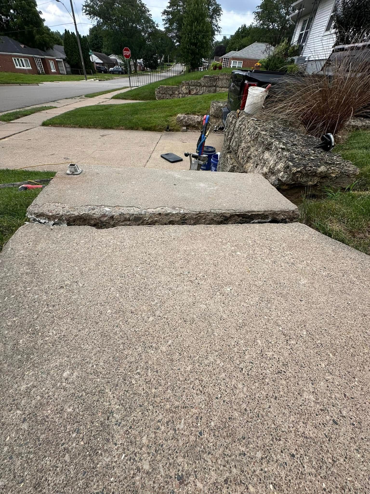 Cracked concrete sidewalk with a significant height difference. Blue tool sits on the elevated section.