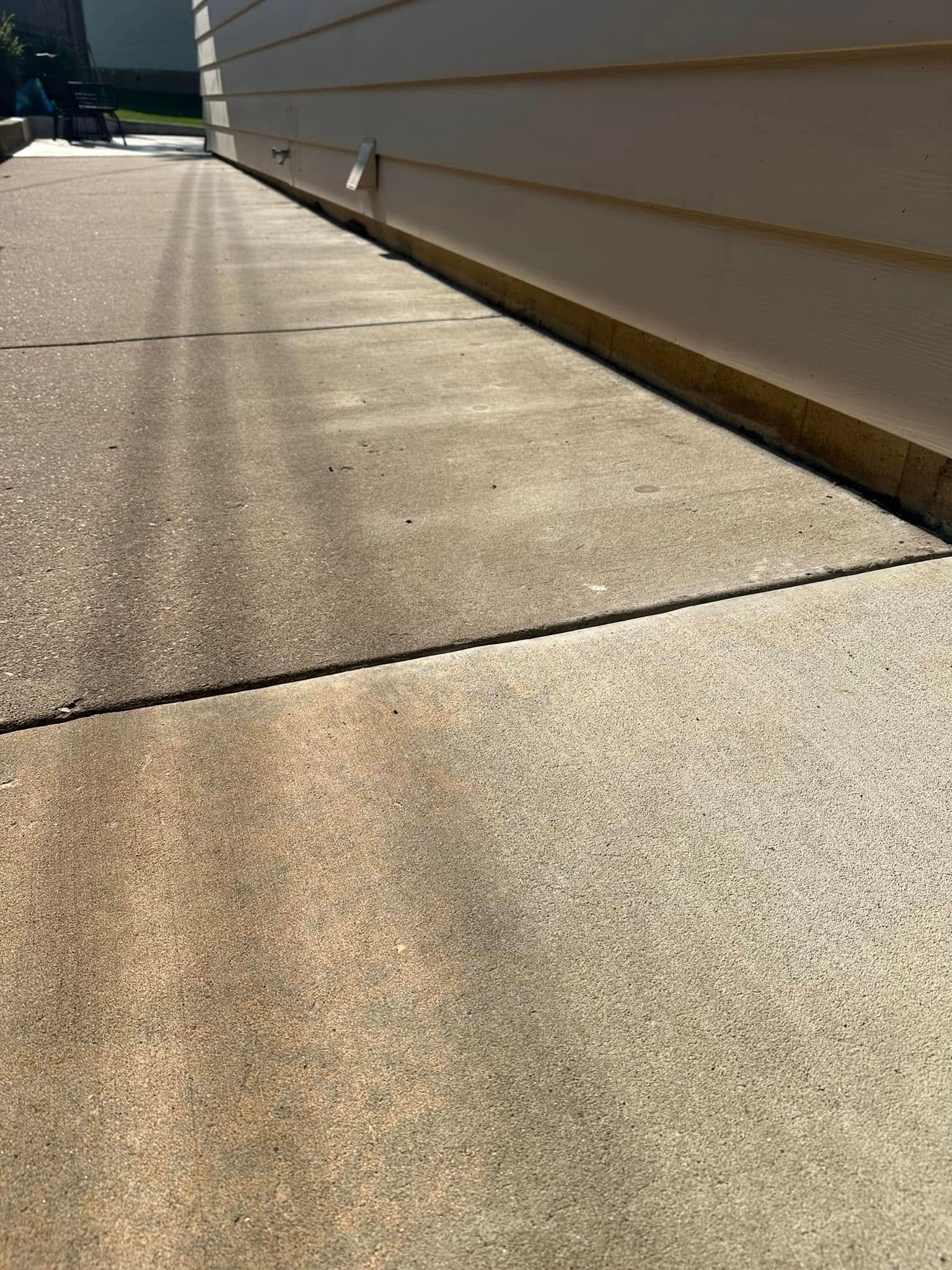 Concrete patio next to a beige building wall, with visible cracks and discoloration.