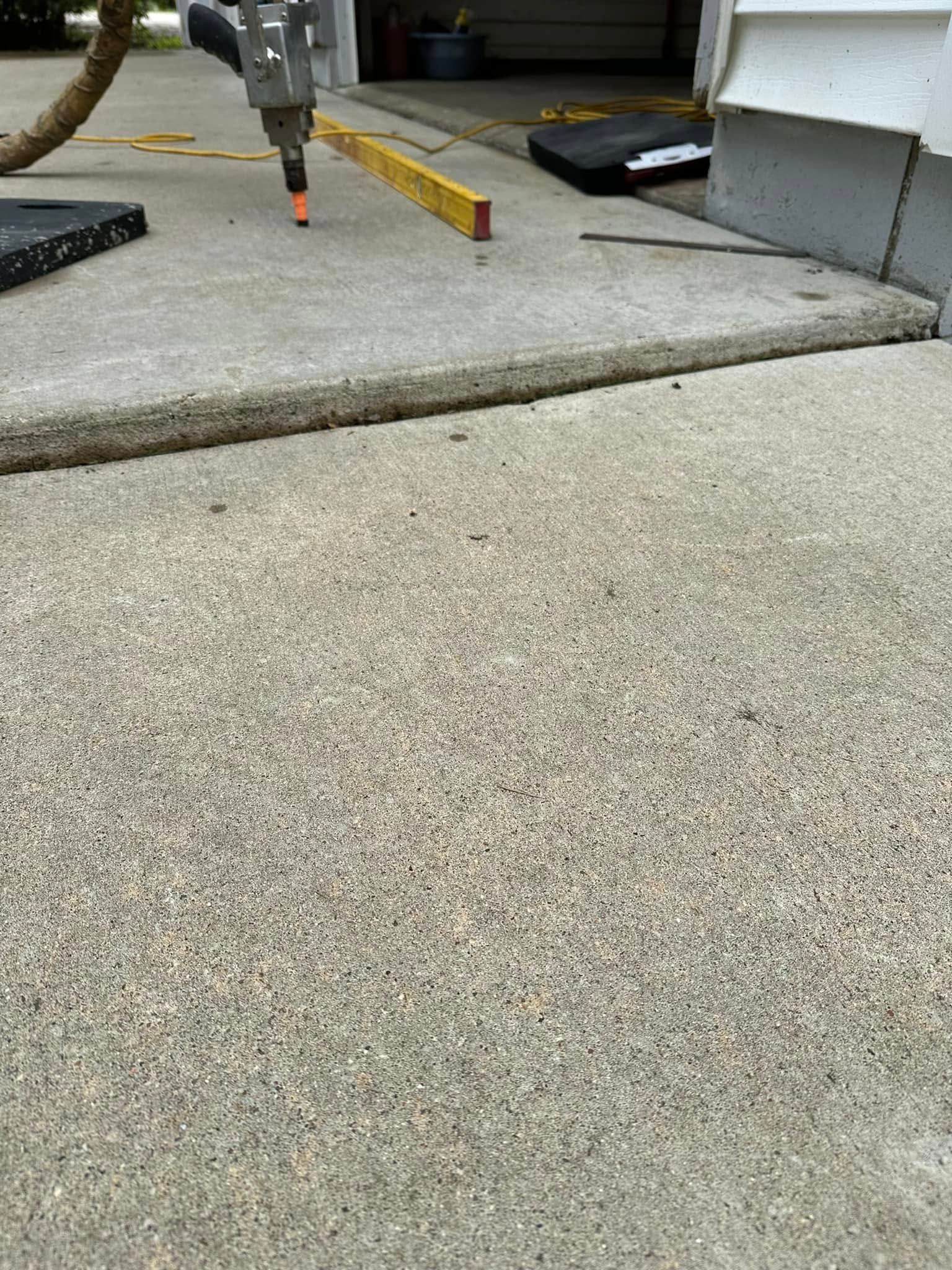 Concrete driveway edge with a large crack, tools in background.