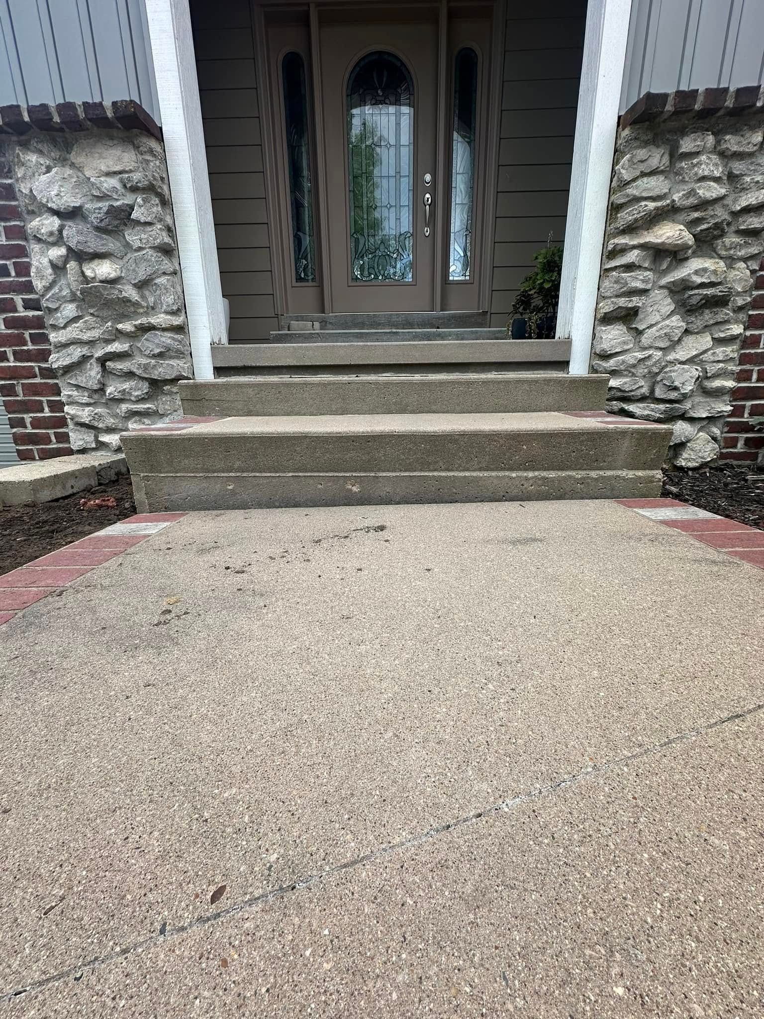 Concrete steps lead to a brown door with glass panels. A pebble walkway is in front of the steps.