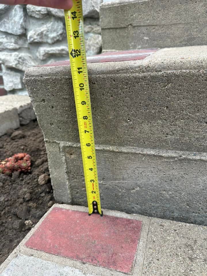 A person measures the height of a concrete step with a yellow tape measure outdoors.