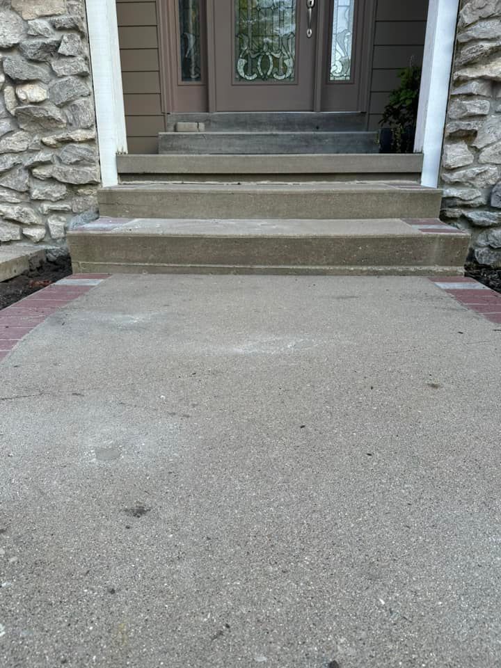 Concrete steps and walkway leading to a brown door with stone columns on either side.