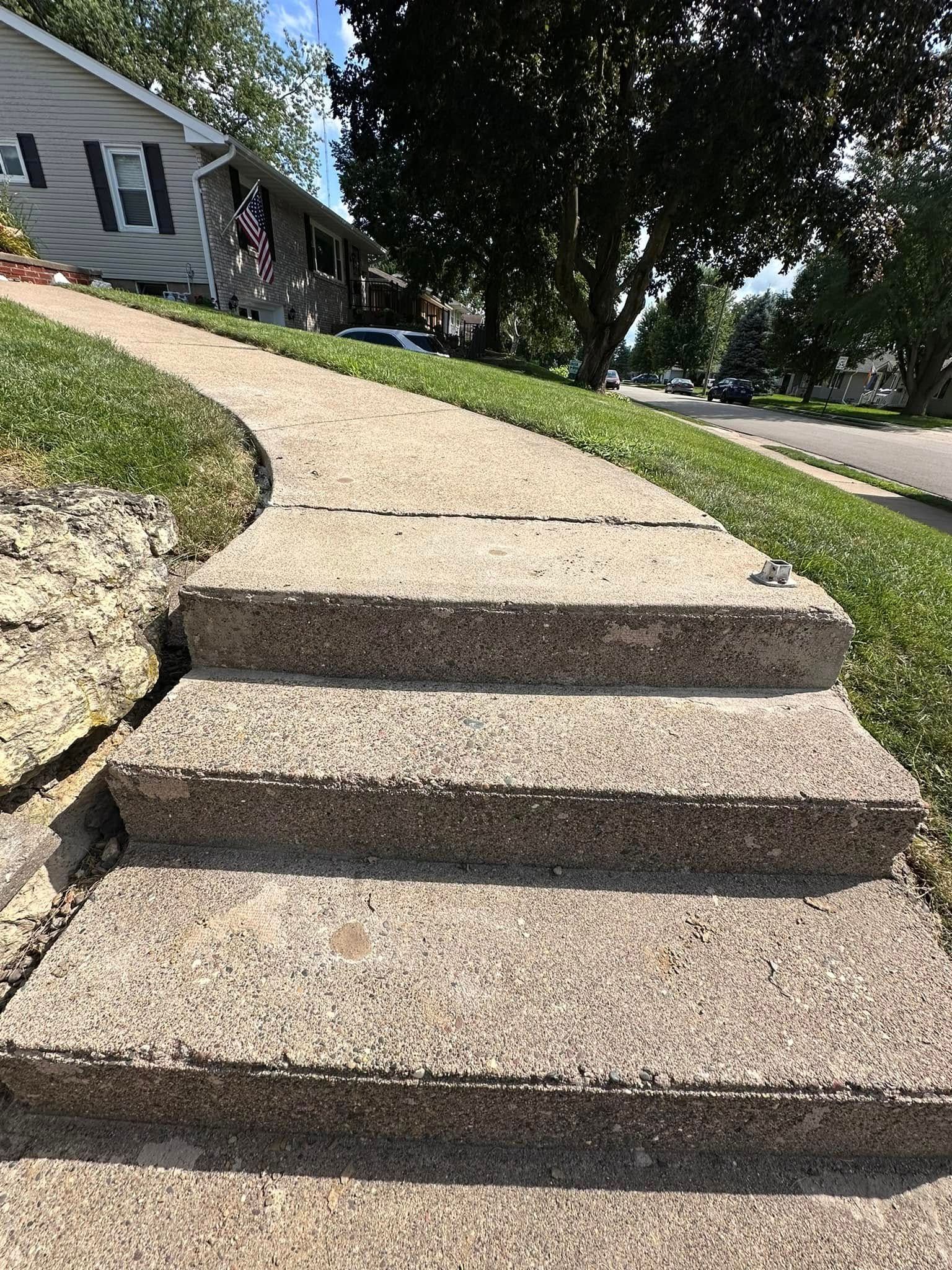 Concrete steps and walkway leading up to a house from a grassy lawn; sunny day.