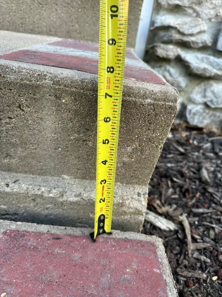 A measuring tape is used to measure the height of a concrete step outdoors.