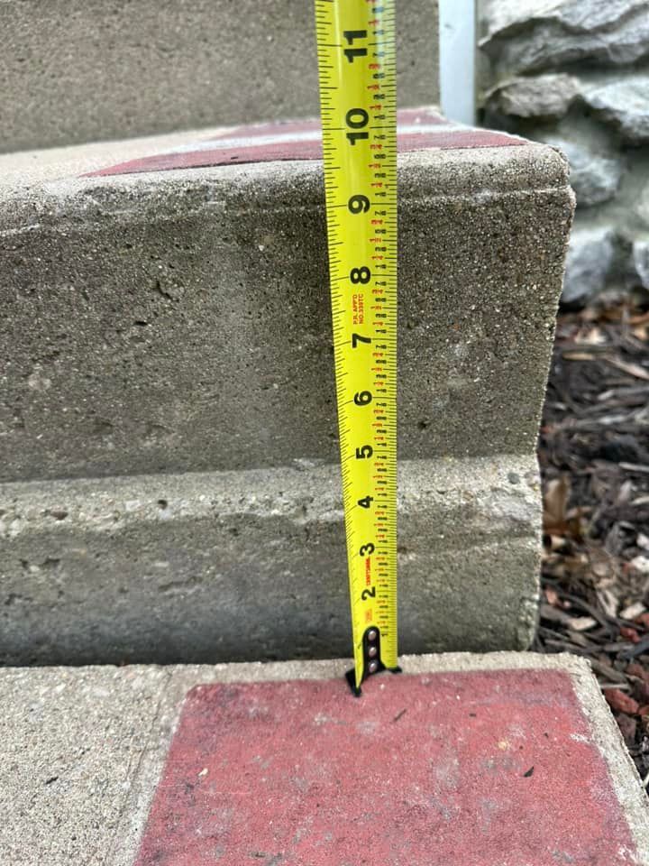 Yellow tape measure measuring a concrete stair step; measurement reads 9 inches.