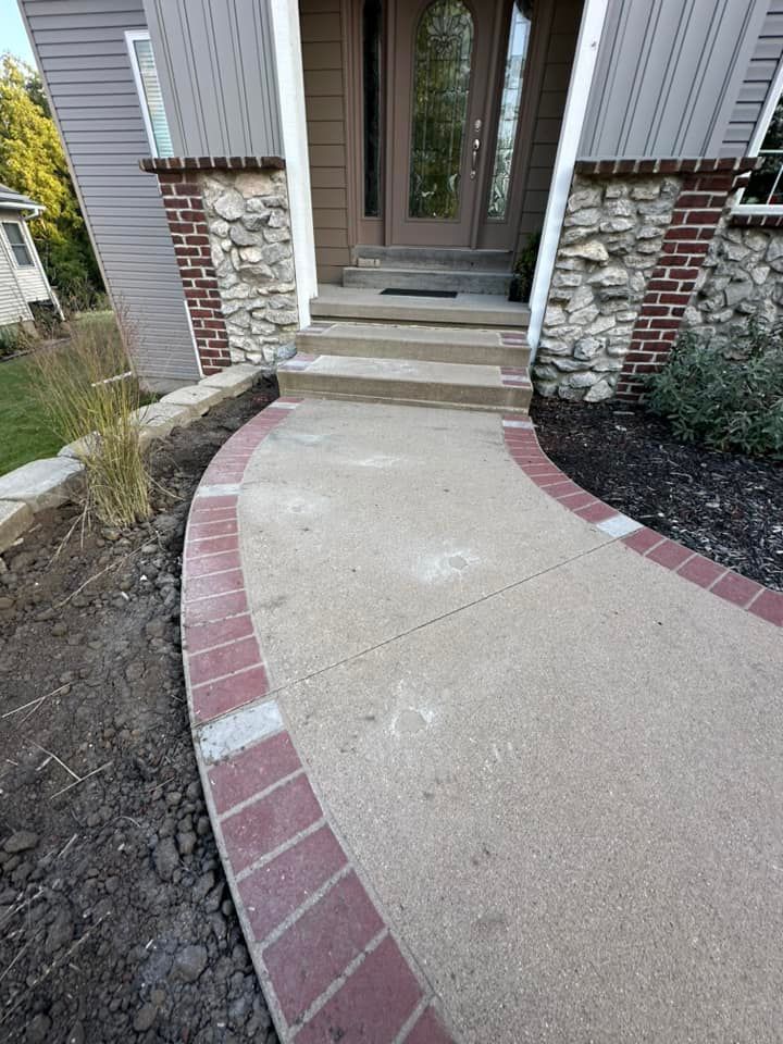 Concrete walkway leading to a house entrance with brick edging and stone accents.