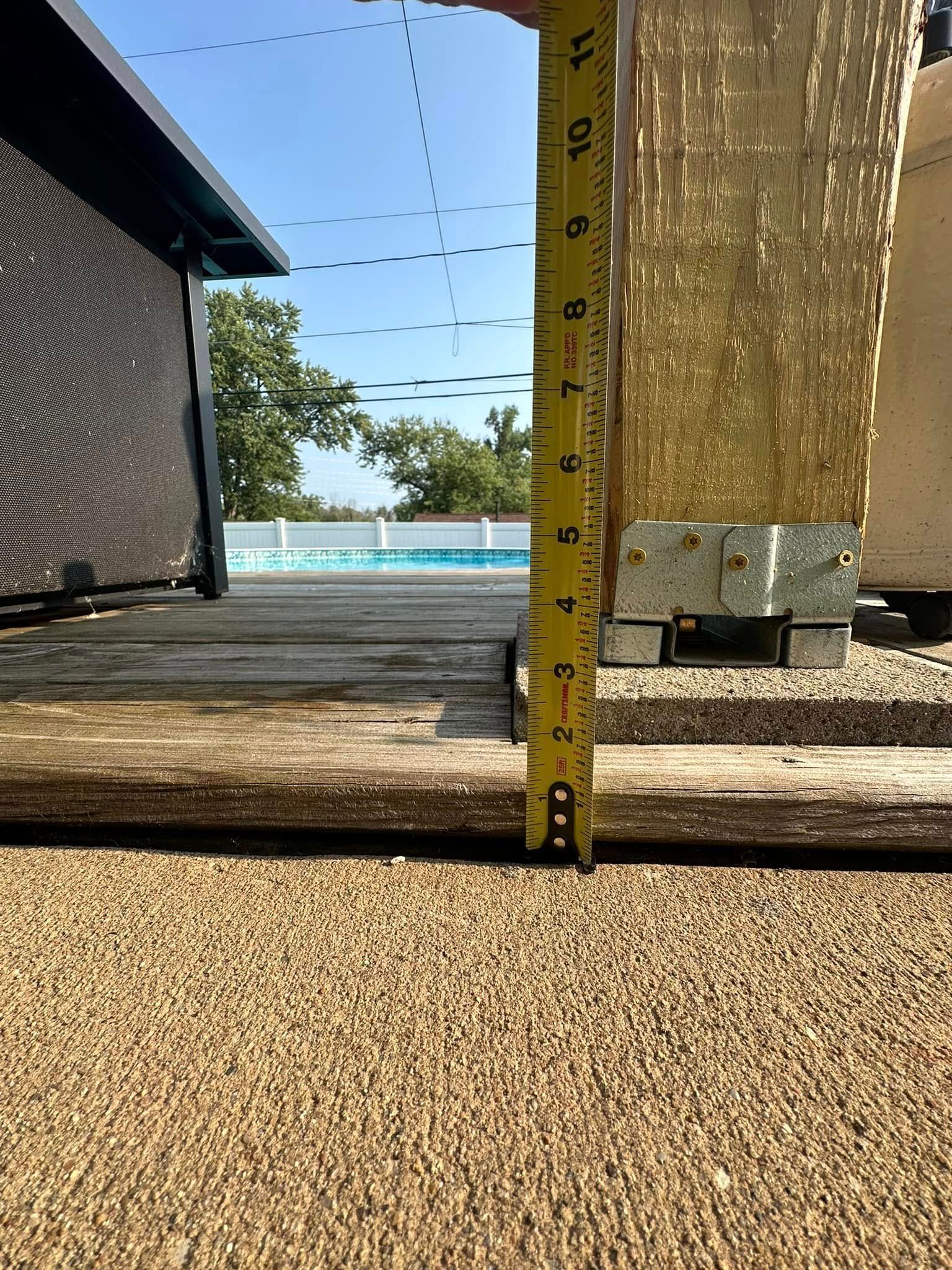Yellow tape measure showing approximately 3 inches from a concrete surface to a wooden deck. Pool and blue sky in background.