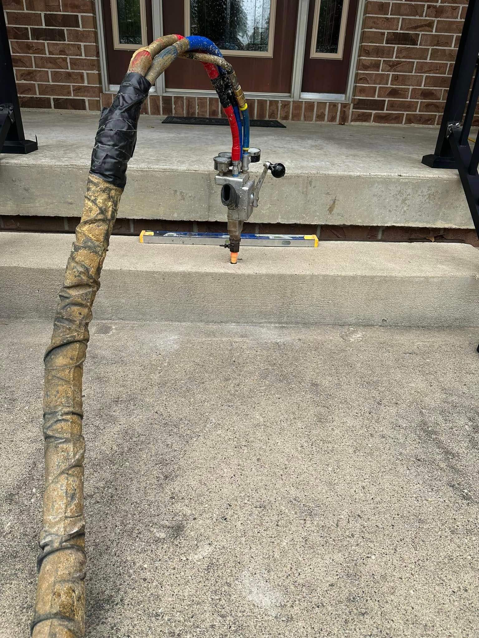 A dirty, wrapped cable attached to a spray gun rests on a concrete surface, in front of a brick building.