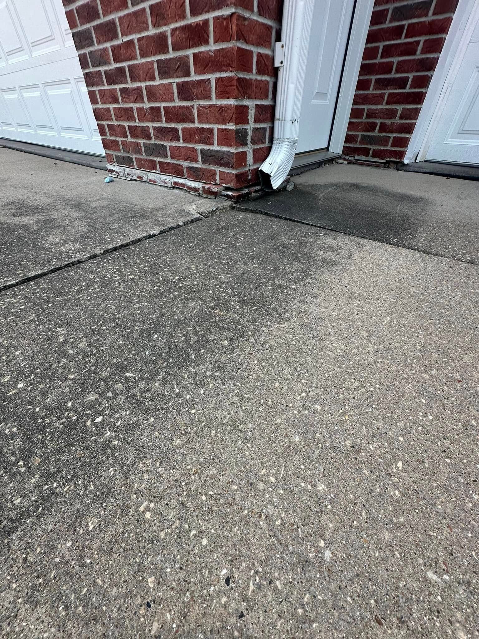 Brick building corner, white garage door, and a concrete driveway.