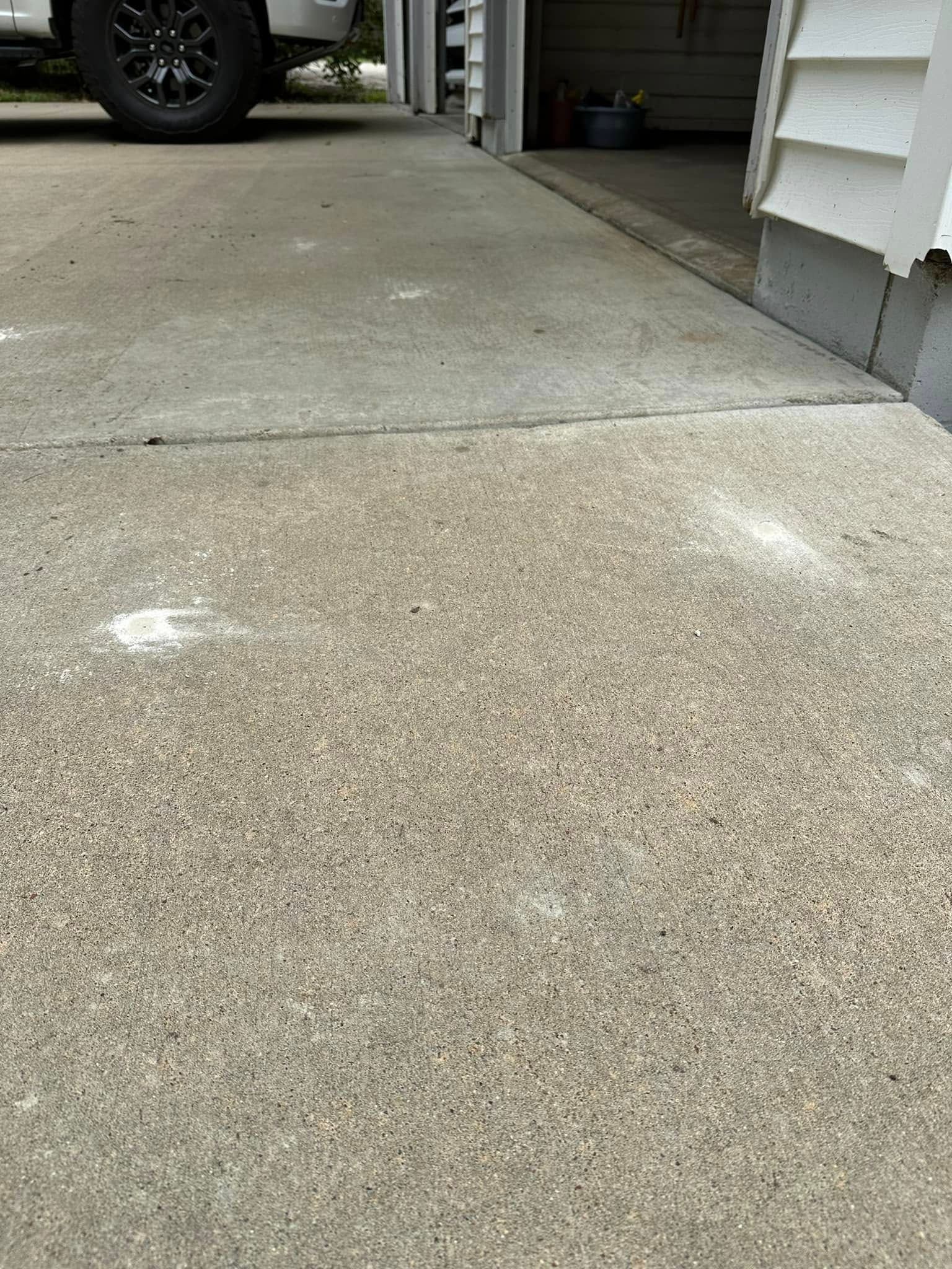 Concrete driveway with white splotches, leading to a garage. A car tire is visible.