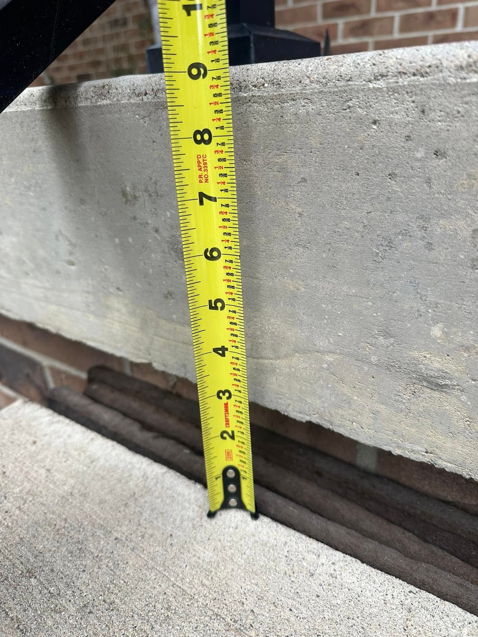 A tape measure showing the height of a concrete structure is approximately 9 inches.