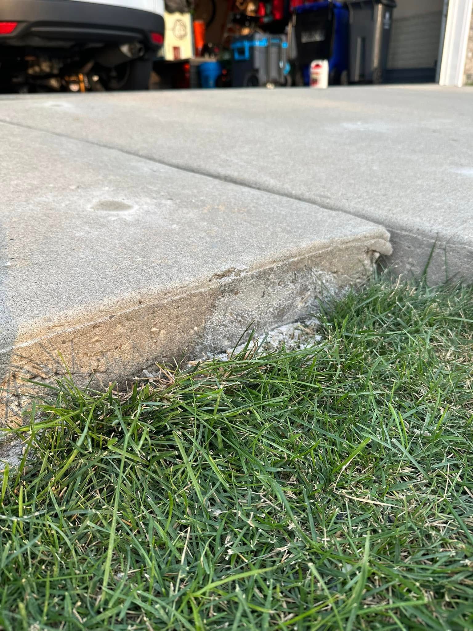 Close-up of a concrete curb edge next to green grass with a garage in the background.