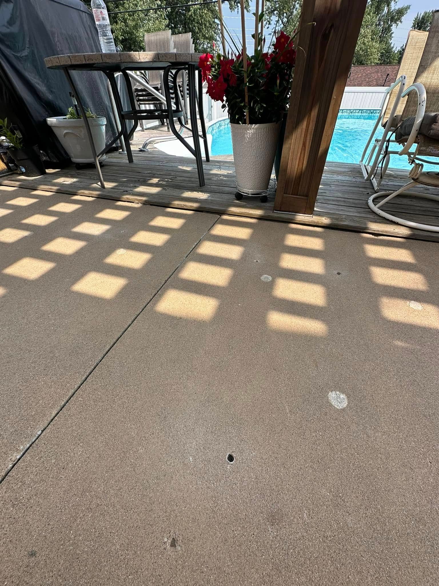 Shadows from a trellis on a concrete patio. Red roses in a white pot, pool in background.