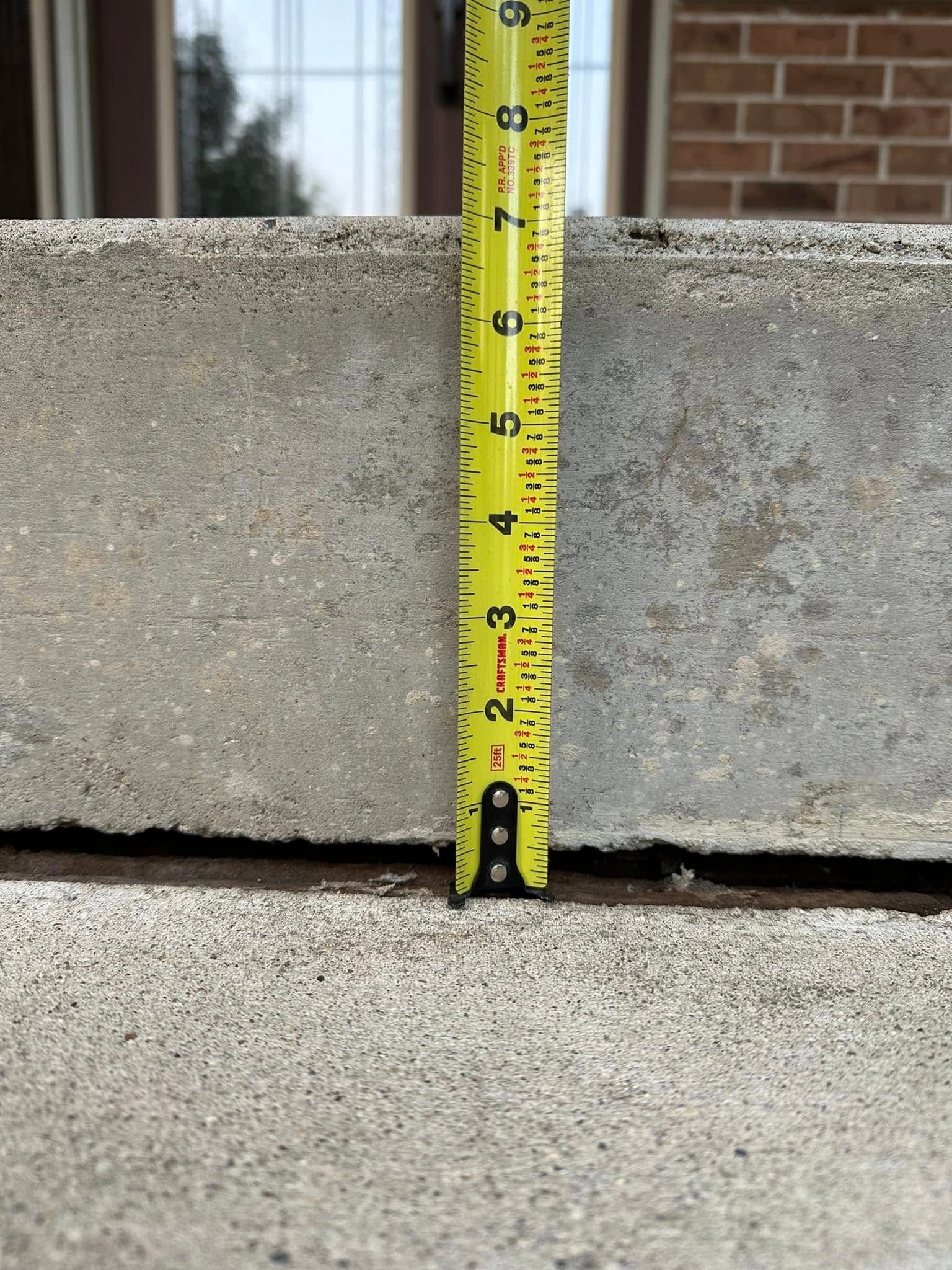Yellow tape measure showing a 2-inch gap between concrete steps. Brown building in background.