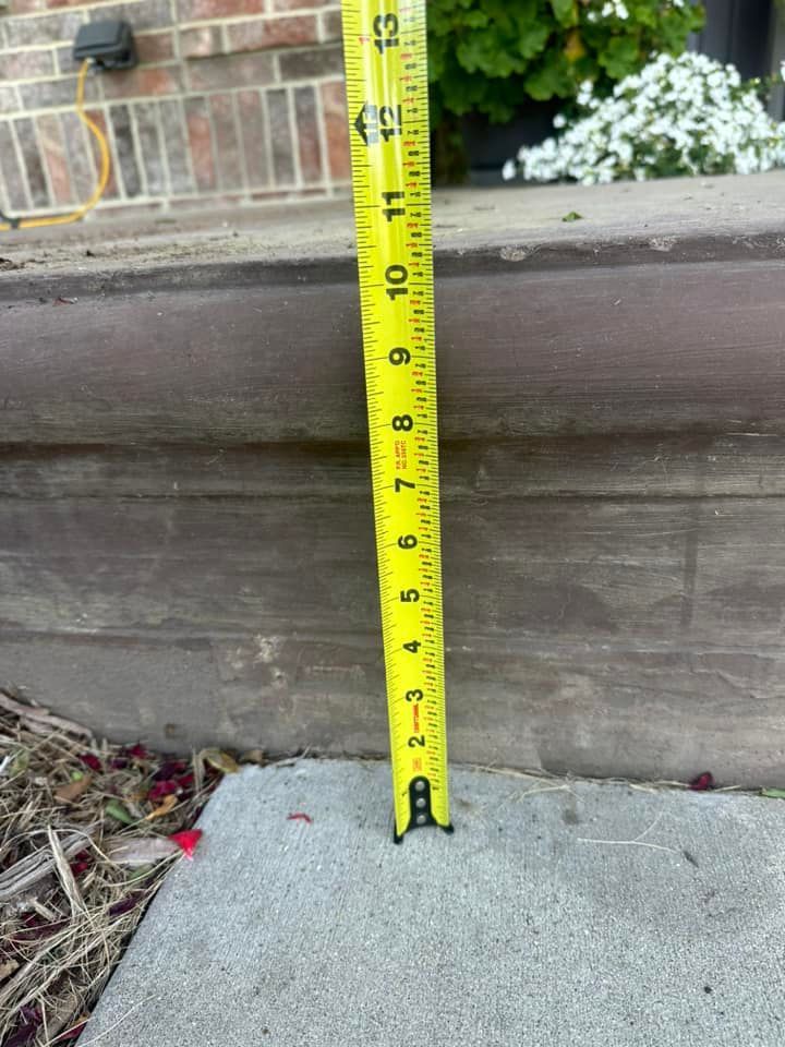 Yellow tape measure vertically measuring a concrete step, appearing to be around 7 inches high.