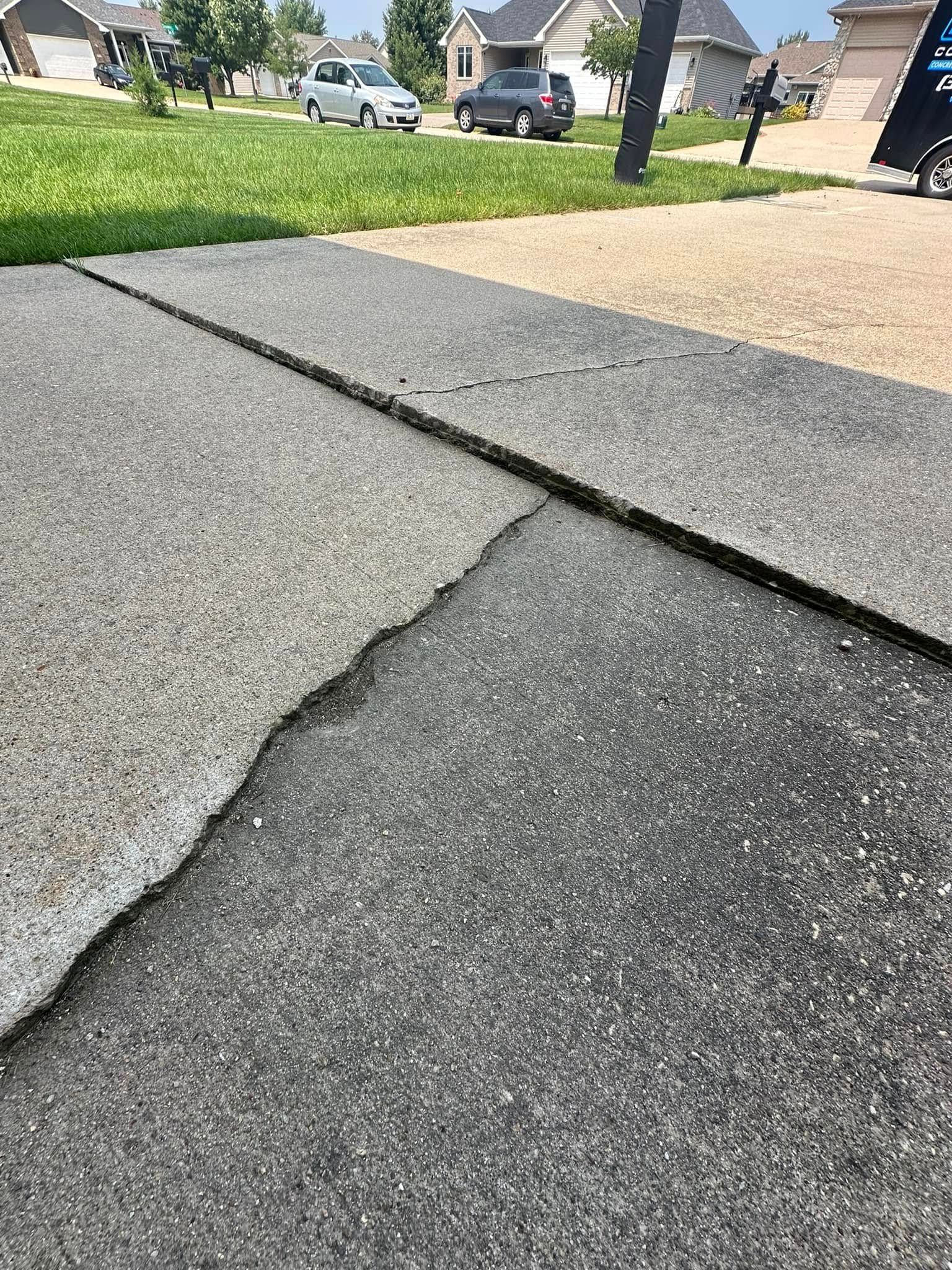 Damaged concrete driveway with a large crack and separation.